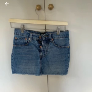 Blå jeanskjol från lager 157 med rå kant - Snygg blå jeanskjol från lager 157 med klassisk femficksmodell, knappar framtill och rå, fransig nederkant. Kjolen har bälteshällor och är i en kort modell som passar perfekt till sneakers eller boots. Tidlös denim-look med coola detaljer.