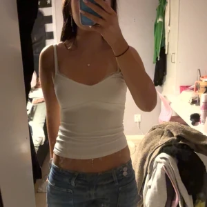 Vit croppad linnetopp med spetskant - Säljer en vit croppad linnetopp med smala axelband och en snygg spetskant längs urringningen. Toppen har en tight passform och är perfekt för dig som gillar en enkel men stilren look. Materialet känns mjukt och stretchigt mot huden.