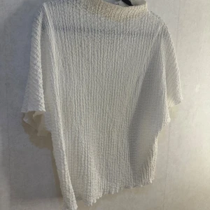 Vit strukturerad topp från Zara - Säljer en vit topp från Zara i storlek S. Bra skick och inga defekter. Toppen har en strukturerad, vågig yta och är tillverkad i ett lätt material. Den har lös passform och korta ärmar, perfekt för varmare dagar. Enkel och stilren design som passar till mycket .