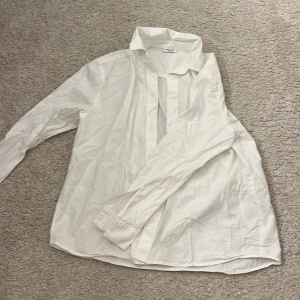 Vit skjorta från Kappahl 146/152 - Klassisk vit skjorta från Kappahl i storlek 146/152. Skjortan har lång ärm, krage och knappar framtill samt vid ärmslut. Tillverkad i mjuk bomull, perfekt för en clean och stilren look. Passar dig som gillar enkel och tidlös stil.