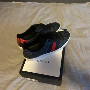 Gucci ace skick 9/10  äkthets bevisade av Vinted  - Gucci sneakers i mörkblått med GG-monogram, röda och blå ränder på sidan och unika hälpaneler i röd och blå ormskinnslook. Vit platt sula med Gucci-logga undertill. Skorna har snörning och är tillverkade i skinn och syntetmaterial.