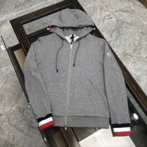 Grå Moncler hoodie med dragkedja - Snygg grå hoodie från Moncler med hel dragkedja, huva med snörning och klassiska Moncler-detaljer. Muddarna har röd, vit och marinblå rand. Perfekt för en chill och sportig look.