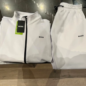 Vita mjukisbyxor från BOSS - Snygga vita mjukisbyxor från BOSS med svart logga på låret. Byxorna har elastisk midja med dragsko och smal passform som sitter tajt vid anklarna. Tillverkade i mjukt och stretchigt material för maximal komfort. Perfekta för en chill och sportig look.