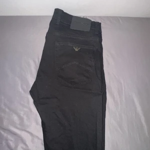 Svarta jeans från Emporio Armani - Snygga svarta jeans från Emporio Armani med klassisk femficksdesign och diskret logga i metall på bakfickan. Jeansen har raka ben och normal passform, tillverkade i mjukt bomullsmaterial med stretch för extra komfort.