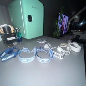 Blå Christian Dior J'Adior armband - Snyggt blått armband från Christian Dior med texten 'J'Adior' broderad i vitt. Armbandet har en bred, vävd design med vita detaljer och avslutas med två tofsar i blått och vitt. Perfekt accessoar för att lyfta din stil. Helt nytt androgs andvänt kan få rabatt desto mera ni köper!