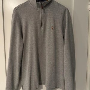 Grå half zip tröja från Polo Ralph Lauren - Snygg grå långärmad tröja från Polo Ralph Lauren med half zip och klassisk broderad logga på bröstet. Tröjan har en ribbad struktur och står ut med sin stilrena design och bekväma passform. Perfekt för dig som gillar enkel och tidlös stil. Tröjan är lite oversized. Vet inte om den är small eller medium. Jag är 181 och sitter bra i längden.