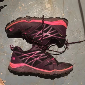 Lila och rosa sneakers från The North Face - Snygga sneakers från The North Face i lila och rosa med svarta detaljer. Skorna har snörning och grov sula som passar perfekt för utomhusaktiviteter. Tillverkade i syntetmaterial och textil, med coola mönstrade skosnören och logga på sidan.