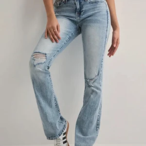 Ljusblå true religion bootcut jeans med slitningar - Säljer ett par ljusblå jeans från True Religion med bootcut passform och snygga slitningar på knäna. Jeansen har klassiska broderade bakfickor och hög midja. Perfekta för dig som gillar en avslappnad men trendig look. 