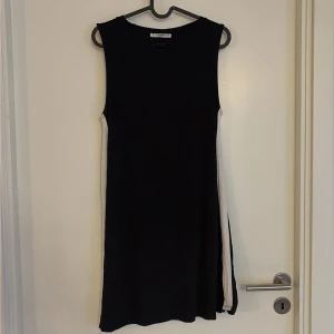 Svart ärmlös klänning Pull&Bear - Svart kortklänning från Pull&Bear i storlek M. Klänningen är ärmlös med rund hals och har en enkel, rak passform. Sidorna har vita paneler som ger en cool kontrast. Perfekt för dig som gillar minimalistisk stil och vill ha något bekvämt och snyggt. Fint använt skick