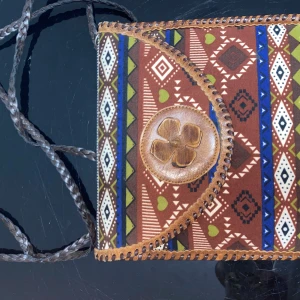 Mönstrad axelväska med skinnblomma - Unik axelväska med färgstarkt etnomönster i brunt, grönt, blått och vitt. Väskan har detaljer i brunt skinn, bland annat en stor blomma på locket och flätad axelrem. Stängs med magnetknapp och har innerfack med dragkedja. Perfekt för dig som gillar boho-stil.