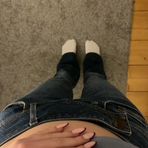 Blå bootcut jeans med låg midja - Säljer ett par blå jeans med snygg tvätt och slitningar, låg midja och bootcut-ben. Jeansen har klassiska fem fickor, dekorativa knappar framtill och kontrastsömmar. Knappast använda och säljer för att dom inte passar mig. Pris kan diskuteras