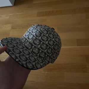 Salvatore Ferragamo mönstrad keps - Snygg keps från Salvatore Ferragamo med grått och svart grafiskt mönster över hela kepsen. Justerbar baktill med band och logodetalj. Kepsen har en klassisk formad skärm och är tillverkad i bomullsmaterial. Perfekt för dig som vill sticka ut med designeraccessoar.