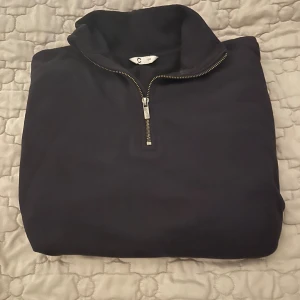 Svart half zip sweatshirt från C - Svart sweatshirt med half zip och hög krage från C. Tröjan har långärmad passform och är tillverkad i mjuk bomull, perfekt för chill dagar. Ribbad nederkant och ärmslut ger en snygg siluett. Enkel och stilren design som funkar till jeans eller mjukis.