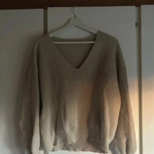 Beige stickad v-ringad tröja - Säljer en beige stickad tröja med v-ringad hals och långärmade, lite oversized ärmar. Tröjan har en ribbad struktur och är perfekt för att mysa i under kyliga dagar. Enkel och stilren design som är lätt att matcha med jeans eller kjol.