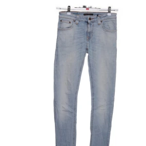  Nudie Jeans  - Säljer ett par ljusblå jeans från Nudie Jeans Co med klassisk femficksdesign och orangea kontrastsömmar. Jeansen har rak passform och är tillverkade i mjukt denimtyg. Perfekta för en avslappnad och stilren look.