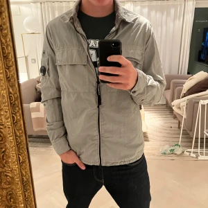 CP Company overshirt - En otroligt snygg CP Company overshirt i jättebra skick. Storlek L men sitter mer som M. Han på bilden är 185 och väger 78. Köptes för 4200 på nk. Materialet är likt en regnjacka och är vattentåligt. Kom privat vid eventuella frågor!