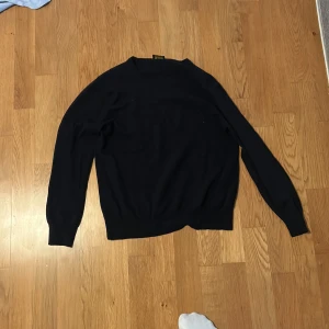 Svart merinoulltröja från Valentino - Svart långärmad tröja från Valentino Roma i 100% merinoull. Klassisk rund halsringning och enkel design som är både stilren och bekväm. Perfekt för dig som gillar exklusiva och tidlösa plagg med mjuk känsla. Nypris 1800