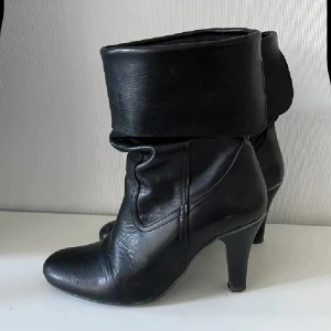 Svarta skinn  stövletter med klack - Snygga svarta stövletter med vikbar skaftkant och smal klack. Skorna har en rund tå och är tillverkade i skinn, vilket ger en stilren och klassisk look. Perfekta för dig som gillar att addera lite edge till outfiten.