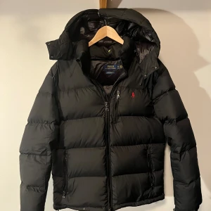 Svart pufferjacka Polo Ralph Lauren - Svårt jacka med Röd logo. Jackan är helt oanvänd nyligen köpt och står i storleken XL men passar mer som en L/M. Extremt mjuk och varm inför vintern och säljs nu billigt. 