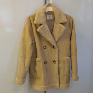 Beige teddyjacka från Zara - JACKA ANVÄND EN ENDA GÅNG. Säljer en beige teddyjacka från Zara med bred krage och dubbla knappar framtill. Jackan har mjukt teddyfoder och detaljer vid krage, fickor, ärmslut och nederkant. Perfekt för dig som gillar chill och cozy vibes under höst och vinter.