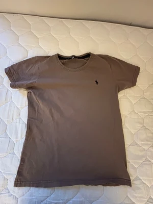 Polo Ralph Lauren T-Shirt - Den här T-shirten kommer i en mjukt brun/beige ton med det klassiska Polo-logotrycket broderat på bröstet. Enkel, clean och passar till allt – perfekt både till vardag och finare tillfällen.  👕 Märke: Polo Ralph Lauren 📏 Storlek: 164 (motsvarar ungefär XS i vuxenstorlek) 🎨 Färg: Brun/beige med svart logga ⭐ Skick: Mycket bra – använd men fint bevarad 📦 Snabb och trygg frakt  En kvalitets-T-shirt med grym passform och stilren design!
