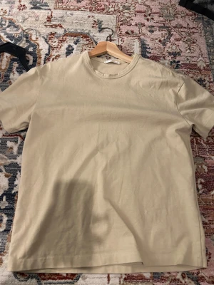 Beige t-shirt från Zara, storlek S - Snygg beige t-shirt från Zara i storlek S. Klassisk rund hals och korta ärmar, tillverkad i mjuk bomull som känns skön mot huden. Enkel och stilren design som funkar till många olika outfits. Perfekt basplagg för garderoben.