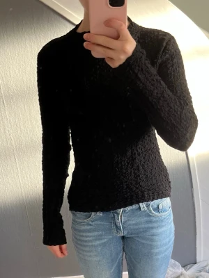 Svart strukturerad tröja från Kappahl - Säljer en svart långärmad tröja från Kappahl med coolt strukturerat tyg. Tröjan har en figurnära passform . Perfekt till jeans eller kjol för en enkel men snygg look.