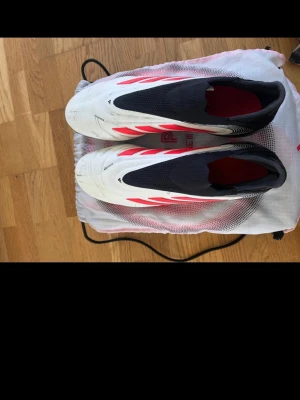 Adidas Copa Pure III fotbollsskor - Adidas Copa Pure III Elite fotbollsskor i vit och svart med röda detaljer. Skorna har en strömlinjeformad design med platt sula och rund tå, samt elastisk ovandel för skön passform. Perfekt för dig som vill ha snygga och funktionella skor på planen. Levereras med originalpåse.