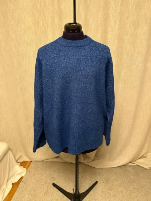 Blå stickad tröja från JJXX - Säljer en chill blå stickad tröja från JJXX i storlek S. Tröjan har loose passform, ribbade muddar vid ärmslut och nederkant samt en liten slits bak. Perfekt för dig som gillar enkel stil med lite extra edge.