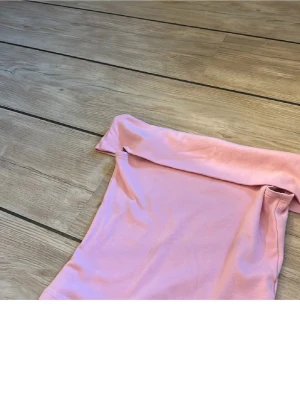 Ljusrosa offshoulder tubtopp - Säljer en ljusrosa tubtopp med offshoulder-design. Toppen är croppad och har en bred kant upptill som ger en snygg och modern look. Materialet känns mjukt och stretchigt, perfekt för dig som gillar bekväma och trendiga plagg.