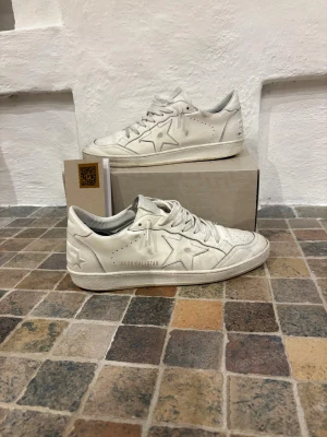 Golden Goose Ballstar  - Golden Goose Ballstar sneakers i helvitt skinn med ikonisk stjärndetalj på sidan och GGDB/BALLSTAR-tryck. Klassisk låg modell med snörning och rund tå. Snygg retrovibe och platt sula med stjärnmönster undertill. Perfekt för dig som gillar exklusiva och stilrena sneakers. Köpts på NK kvitto finns.