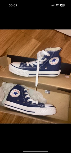 Converse All Star navy high-tops - Säljer ett par klassiska Converse All Star high-tops i marinblått med vit sula och vita snören. Skorna har rund tå, platt sula och det ikoniska All Star-märket på sidan. Materialet är slitstark canvas och sulan är i gummi. Perfekt för dig som gillar streetstyle.