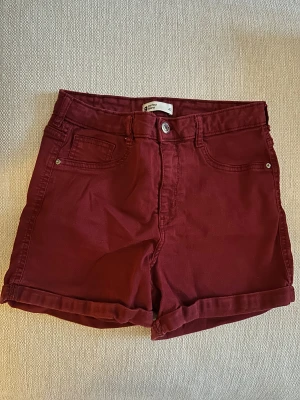 Vinröda jeansshorts - Snygga vinröda jeansshorts från ginatricot i klassisk femficksmodell. De har hög midja, uppvikta benslut och knapp- samt dragkedjestängning framtill. Materialet är mjuk bomull med lite stretch för extra komfort. 