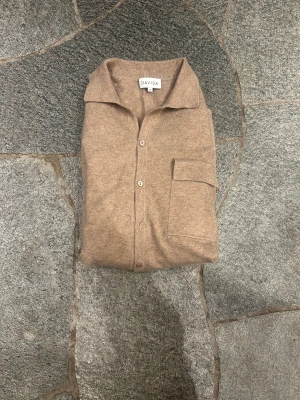 Beige kashmirkofta från Davida  - Supermjuk 100% kahsmir beige kofta från Davida. Klassisk modell med krage, knäppning framtill och en bröstficka. Långärmad och ribbade muddar. Perfekt för lager-på-lager. Notera att en knapp har gått av vilket man enkelt kan fixa hos en skomakare eller liknade (bild 3) Nypris: 3299 
