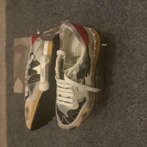 Valentino Garavani Rockrunner sneakers - Helt nya Valentino Garavani Rockrunner sneakers med camouflagemönster i svart, grått och vitt, samt röda detaljer vid hälen. Extra snören ingår.