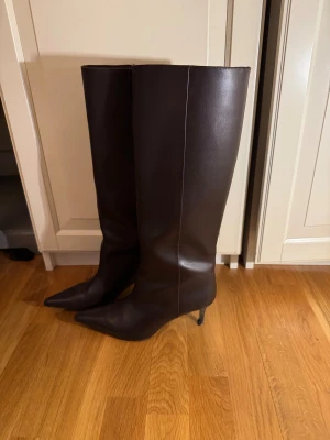 Bruna höga stövlar med spetsig tå - Snygga, höga bruna stövlar i skinn med spetsig tå och smal klack. Klassisk och stilren design som passar till många outfits. Stövlarna har en elegant siluett och är perfekta för dig som gillar en chic look. Sista bild, dess enda defekt.                     Nypris: 599 H&M