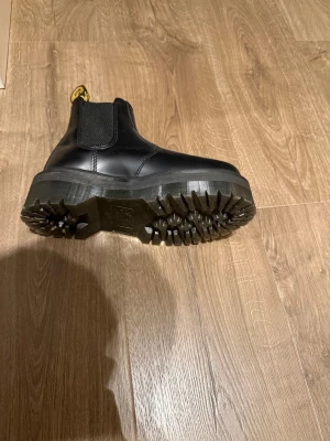 Dr. Martens svarta Chelsea boots - Säljer ett par svarta Dr. Martens Chelsea boots med grov platt sula och klassisk gul söm runt sulan. Skorna har elastiska paneler på sidorna och en dragflik med logga bak. Tillverkade i skinn med rund tå och robust plattform för extra edge.