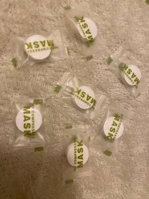 DIY komprimerade ansiktsmasker - Säljer flera DIY komprimerade ansiktsmasker i individuella plastförpackningar. Maskerna är vita och runda, tillverkade av mjukt material som expanderar med vätska. Perfekt för att använda med toner eller face mist för en fräsch känsla.
