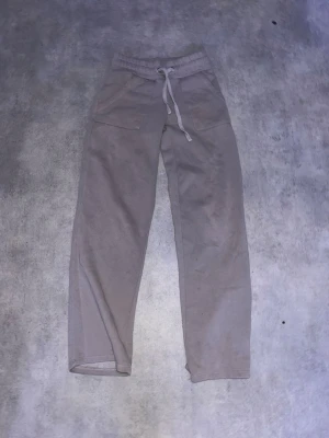 Grå mjukisbyxor med snörning - Grå mjukisbyxor med bred resår i midjan och snörning framtill. Byxorna har raka ben och två stora fickor framtill. Perfekta för chill dagar eller när du vill vara bekväm. Tillverkade i mjukt bomullsmaterial. OBS! har ett litet hål där bak