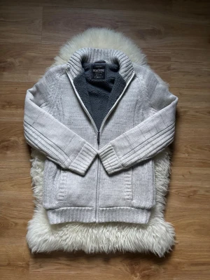 Peacocks kofta - Säljer en ljusgrå stickad kofta från Peacocks i storlek small. Koftan har dragkedja framtill, ribbade muddar och krage samt ett mjukt grått fleecefoder på insidan. Perfekt för kyliga dagar med sin mysiga och värmande känsla. PRISET KAN DISKUTERAS!