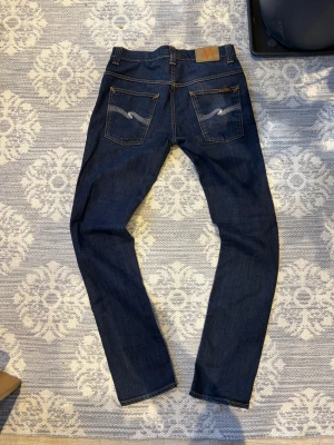 Nudie Jeans Thin Finn blå jeans - Säljer ett par mörkblå jeans från Nudie Jeans i modellen Thinn finn. Klassisk femficksdesign och orangea kontrastsömmar. Mycket fins skick hör av er om ni har några frågor MVH theo