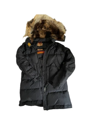 Svart dunjacka Parajumpers - Säljer en svart Parajumpers dunjacka med avtagbar huva och äkta päls. Jackan har flera fickor, dragkedja och coola detaljer som patch på ärmen. Denna modell har jag använt som xs/s även fast de står Young. Modellen finns inte längre att få tag på då de är den mindre oranga rämmen på denna jacka!🌟