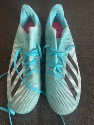  Adidas fotbollsskor  -  turkosa Adidas fotbollsskor med svarta ränder på sidorna och vita dobbar undertill. Perfekta för dig som vill sticka ut på planen.