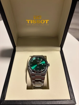 Grön Tissot PRX klocka med stållänk - Snygg Tissot PRX klocka med grön urtavla och stilren stållänk. Klockan har minimalistisk design, datumfunktion och silverfärgade detaljer. Perfekt accessoar för dig som gillar klassisk men modern stil. Levereras i original ask med guldfärgad logga.