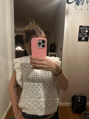 Vit stickad ärmlös topp från ONLY - Supersöt vit stickad topp från ONLY med volangdetaljer på axlarna och ett fint hålmönster över hela plagget. Toppen är ärmlös och har en rund halsringning, perfekt för en fräsch och trendig look.