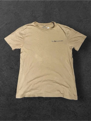 Beige t-shirt från Polo Ralph Lauren - Snygg beige t-shirt från Polo Ralph Lauren med diskret logga på bröstet. Klassisk rund hals och korta ärmar. Tillverkad i mjuk bomull som känns skön mot huden. Perfekt för en chill och stilren look.