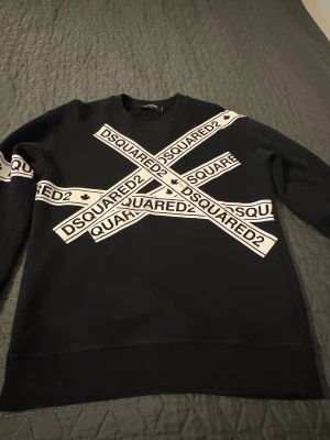 Svart tröja  från Dsquared2  - Svart sweatshirt från Dsquared2 i storlek S med vita bandtryck över bröstet och ärmen där det står DSQUARED2. Tröjan har rund hals, lång ärm och är gjord i mjuk bomull med insida i fleece. Snygg och streetig look med tydlig logga framtill.