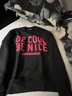 Svart Dsquared2 sweatshirt S - Svart sweatshirt från Dsquared2 i storlek S med fet rosa text 'BE COOL BE NICE' på framsidan. Rund hals, ribbade muddar och mjukt material som känns skönt mot huden. Perfekt statement-plagg för dig som gillar streetstyle och vill sticka ut på ett tyst sätt. Sälja för att jag aldrig riktigt passade med den. Jag var för smal och ärmarna var för långa (183cm, 60kg)