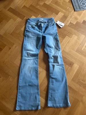 Lågmidjade Bootcut ljusblå jeans från Nelly - Snygga ljusblå bootcut jeans från Nelly med klassisk femficksdesign och dubbla knappar fram. Baktill finns coola fickor med röd och vit zigzag-söm som ger extra attityd. Jeansen har låg midja och är tillverkade i mjukt denimtyg.
