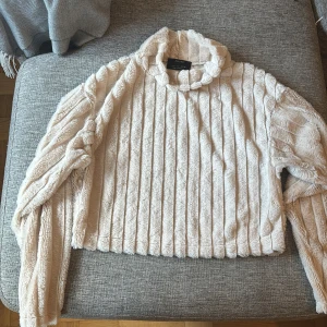 Beige fluffig tröja från Bershka - Supermjuk och fluffig beige tröja från Bershka i storlek S. Tröjan har lång ärm, hög krage och ett ribbat mönster som ger en mysig vibe. Perfekt för kyliga dagar när du vill vara både bekväm och snygg.